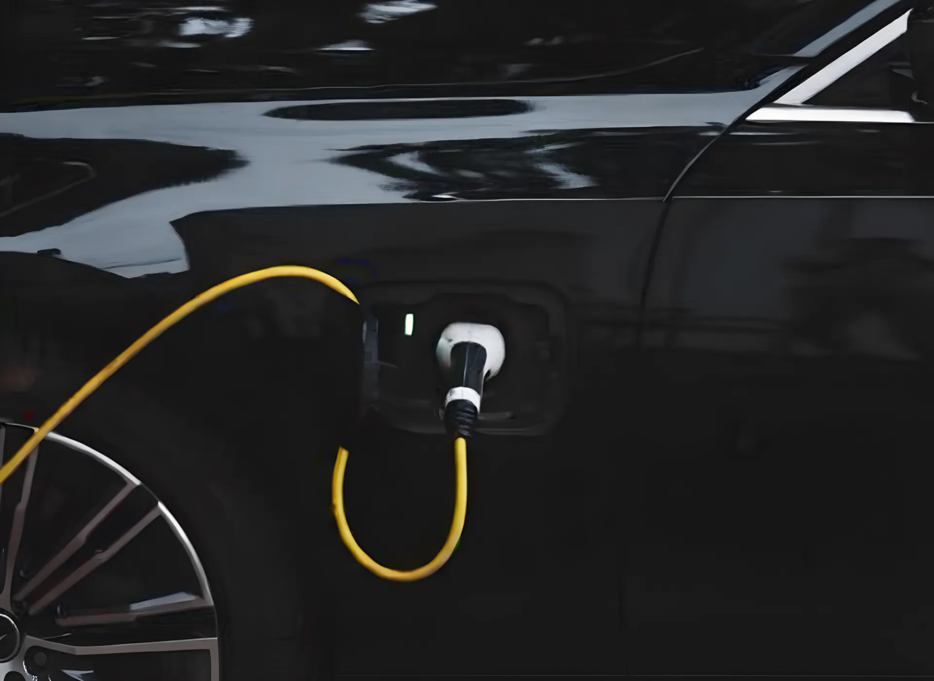 Close-up of a black electric car plugged in to charge with a bright yellow cable